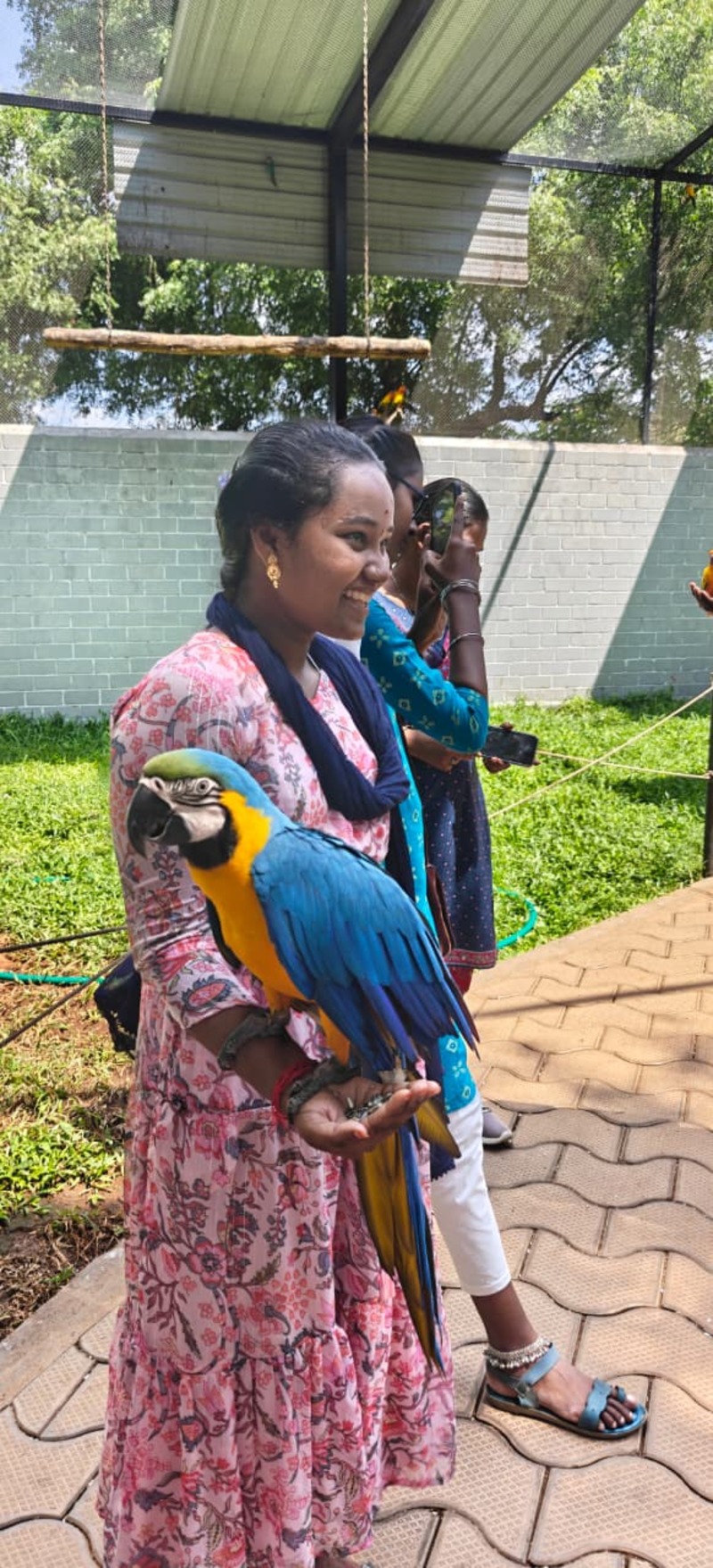 A vision-disabled student from Thaaikarangal Charitable Trust smiles as she gently holds a blue-and-yellow macaw during the field trip. Surrounded by fellow participants, the student experiences the bird's presence through touch, feeling its weight, feathers, and movements, reflecting the joy and emotional connection fostered through this immersive interaction with nature. A vision-disabled student from Thaaikarangal Charitable Trust smiles as she gently holds a blue-and-yellow macaw during the field trip. Surrounded by fellow participants, the student experiences the bird's presence through touch, feeling its weight, feathers, and movements, reflecting the joy and emotional connection fostered through this immersive interaction with nature.