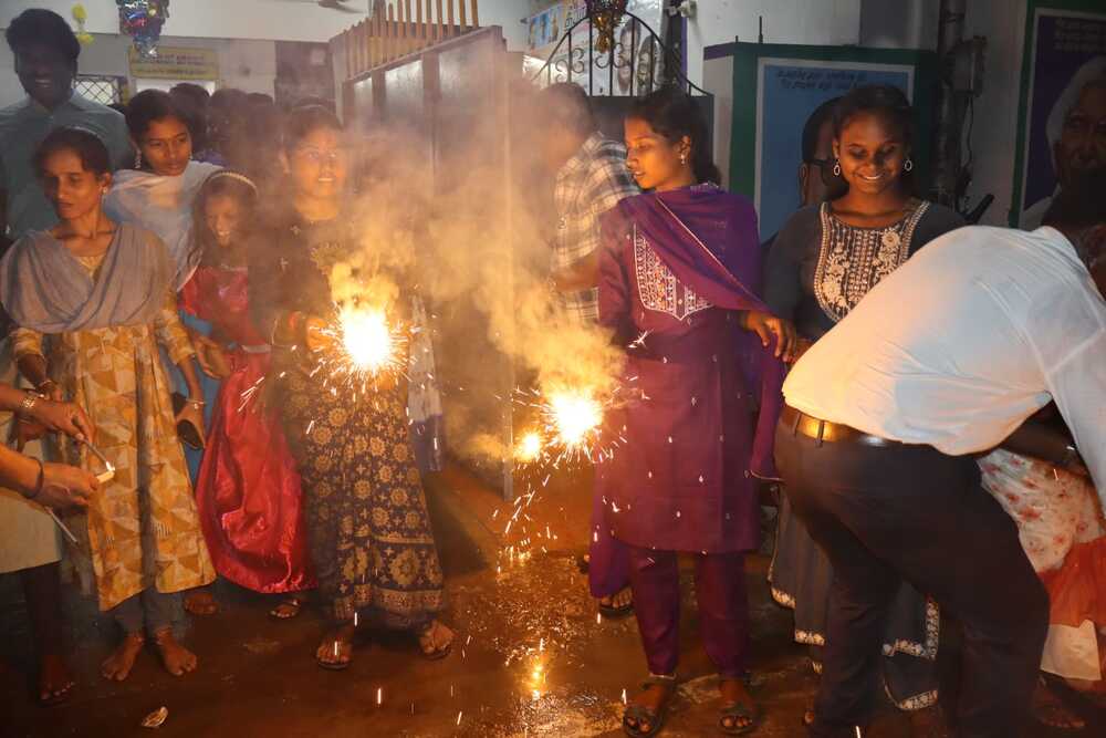 Young beneficiaries celebrate Diwali with glowing sparklers, surrounded by volunteers and friends in a lively festive atmosphere at Thaaikarangal Charitable Trust.