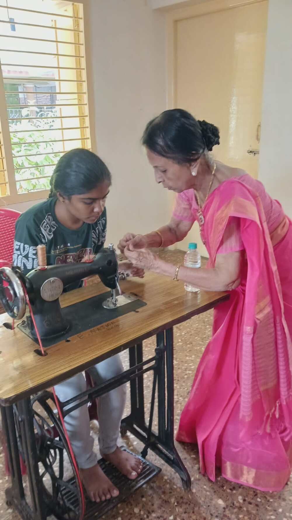 A trainer provides hands-on guidance to a visually impaired participant learning to operate a sewing machine during the residential tailoring training camp. A trainer provides hands-on guidance to a visually impaired participant learning to operate a sewing machine during the residential tailoring training camp.